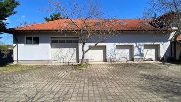 Mehrere Garagen und ein gepflasterter Vorplatz vor dem Gebäude unter blauem Himmel.