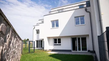 Moderne Reihenhäuser mit kleinen Gärten und Terrassenzugang unter blauem Himmel.