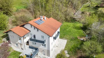 Luftaufnahme eines modernen Wohnhauses mit Ziegeldach und Photovoltaikanlage, umgeben von viel Grün.