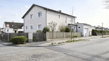 Einfamilienhaus an einer Straßenecke mit gepflegtem Vorgarten und Holzzaun.