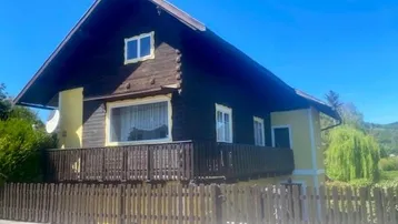Traditionelles Haus mit Holzbalkon und gelber Fassade unter blauem Himmel.