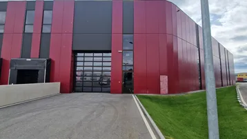 Modernes Industriegebäude mit roter und schwarzer Fassadenverkleidung sowie großen Rolltoren und Zufahrt.