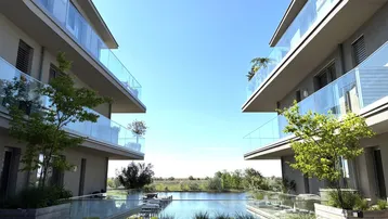 Moderne Wohngebäude mit Glasbalkonen und Blick auf einen ruhigen See unter blauem Himmel.