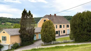 Gelbes Landhaus mit grünen Fensterläden und weitem Blick über die hügelige Landschaft.