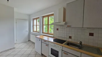Helle Küche mit weißen Fliesen, Holz-Arbeitsplatten und Blick ins Grüne.