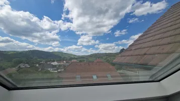 Panoramablick aus einem Dachfenster über Dächer, grüne Hügel und eine weite Landschaft.