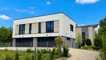 Moderne Architektur mit weißer und grauer Fassade, großen Fenstern und Garagenzufahrt unter blauem Himmel.