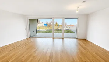 Helles, leeres Wohnzimmer mit Holzboden und Zugang zu einer Terrasse oder einem Balkon.