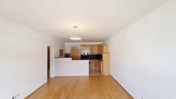 Helles Wohnzimmer mit Parkettboden und offener Küche, durch eine Theke abgetrennt.
