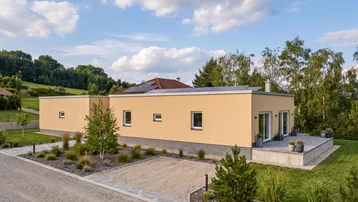 Modernes Einfamilienhaus mit gelber Fassade, Flachdach mit Solaranlage und gepflegter Außenanlage aus der Vogelperspektive.