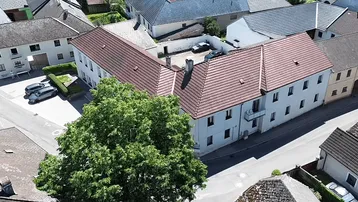 Luftaufnahme eines Gebäudekomplexes mit roten Ziegeldächern und umliegender ländlicher Bebauung.