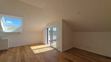 Helles Zimmer im Dachgeschoss mit Holzboden, Dachfenster und Zugang zu einem Balkon.