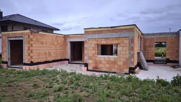 Rohbau eines Einfamilienhauses mit Ziegelwänden und vorbereiteten Fensteröffnungen in ländlicher Umgebung.