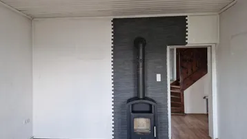 Gemütlicher Raum mit Holzofen, dekorativer Wandverkleidung und Zugang zur Holztreppe.