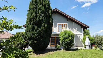 Freistehendes Haus mit großem Garten, hohen Bäumen und Außengrillplatz unter blauem Himmel.