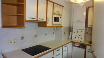 Helle Küche mit weißen Schränken, Holzrahmen, Kochfeld und integriertem Backofen.