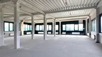 Großer, offener Büroraum im Rohbau mit vielen Fenstern und Blick ins Grüne.