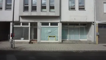Fassade eines Geschäftsgebäudes mit leerstehenden Ladenflächen und Obergeschossfenstern, die zur Vermietung stehen.