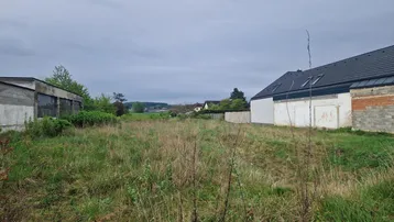 Weitläufiges, unbebautes Grundstück mit Grasfläche und Blick auf umliegende Gebäude unter bewölktem Himmel.