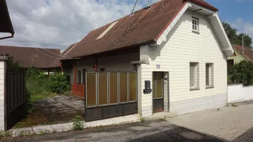 Vorderansicht eines älteren Hauses mit weißer Fassade, braunem Dach und Einfahrt.