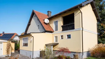 Rückansicht des gelben Hauses mit Loggia, Satteldach und Solaranlage auf Nebengebäude.