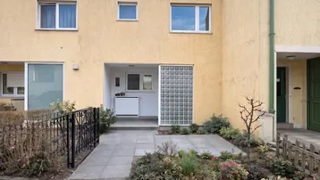 Gelbe Fassade eines Reihenhauses mit Eingangsbereich, Fenstern, kleinem Vorgarten und Glasbausteinwand.