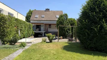 Gepflegter Gartenbereich mit Rasenfläche, hohen Hecken, kleinem Pool und überdachter Terrasse.