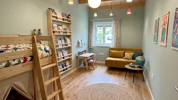 Helles Kinderzimmer mit Hochbett, Holzbalkendecke und farbenfroher Dekoration.