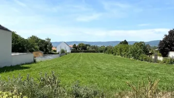 Große grüne Wiese mit weitem Blick auf die umliegende Landschaft und entfernte Berge unter blauem Himmel.