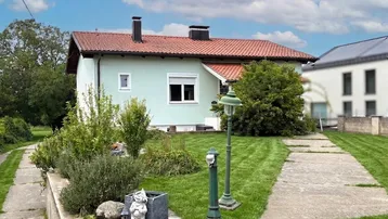 Einfamilienhaus mit hellgrüner Fassade, rotem Ziegeldach und gepflegtem Vorgarten.