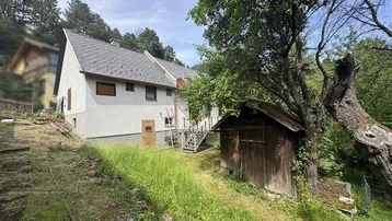 Hausfassade mit angrenzendem Gartenbereich und einem kleinen Holzschuppen in ländlicher Umgebung.