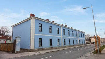 Blau gestrichenes Mehrfamilienhaus an einer Straße unter einem klaren Himmel.