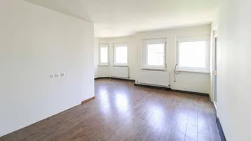 Helles, leeres Zimmer mit Holzoptikboden und mehreren Fenstern, bereit zur individuellen Gestaltung.