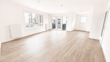 Helles, leeres Wohnzimmer mit Laminatboden, großen Fenstern und Zugang zu einem Balkon.