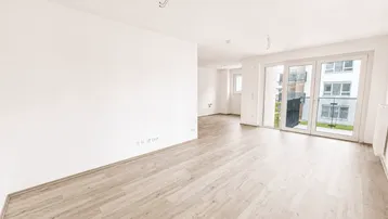 Heller, leerer Wohnbereich mit großen Schiebetüren zum Balkon und modernem Laminatboden.