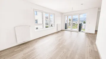 Heller, unmöblierter Wohnbereich mit großen Fenstern, Laminatboden und Zugang zur Terrasse.
