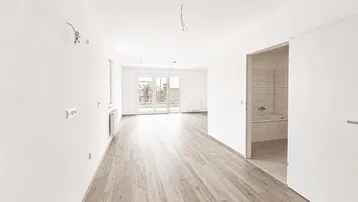 Helles, leeres Zimmer mit Laminatboden und Zugang zu einem Balkon oder einer Terrasse.