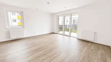 Helles, leeres Zimmer mit Laminatboden und Zugang zu einem Balkon, ideal als Wohn- oder Schlafzimmer.