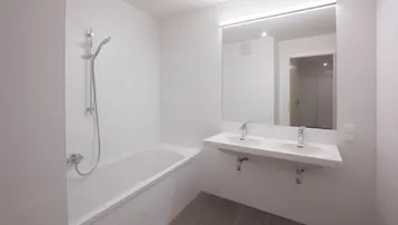 Modernes Badezimmer mit Badewanne, Doppelwaschbecken und großen grauen Bodenfliesen.