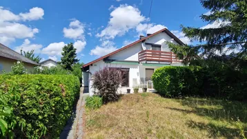 Einfamilienhaus mit weißer Fassade, Balkon und gepflegtem Vorgarten unter blauem Himmel.