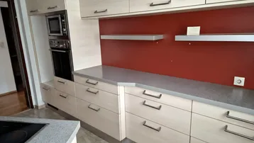 Moderne Küche mit hellen Holzfronten, grauer Arbeitsplatte und integrierten Geräten für den täglichen Gebrauch.