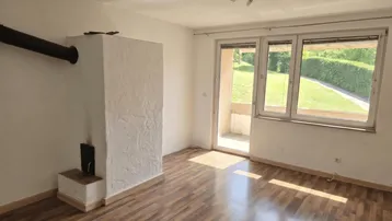 Geräumiges Wohnzimmer mit Kaminofen, Laminatboden und Zugang zu einem sonnigen Außenbereich.