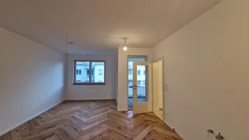Helles Zimmer mit Fischgrätparkett und Zugang zu einem Balkon oder einer Terrasse.