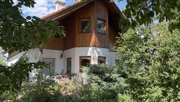 Charmantes Haus mit Holzverkleidung und weißer Fassade, umgeben von üppigem Grün.