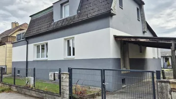 Vorderansicht eines Einfamilienhauses mit zweifarbigem Anstrich und Mansarddach.