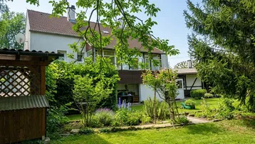 Großzügiger Gartenbereich hinter dem Haus mit viel Grün, Bäumen und einem kleinen Holzschuppen.