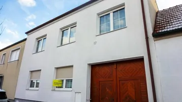 Weiß verputztes Haus mit großen Holztoren und Rollläden an den Fenstern.