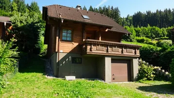 Traditionelles Holzhaus mit Balkon und integrierter Garage in grüner Hanglage.