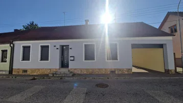 Frontansicht eines renovierten Einfamilienhauses mit grauer Fassade und Rollläden unter strahlendem Sonnenschein.