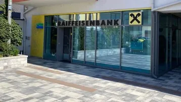 Eingangsbereich einer modernen Bankfiliale mit großer Glasfassade und gepflastertem Vorplatz.